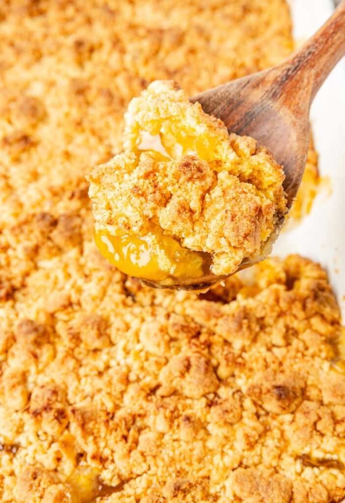 A baking pan of peach cobble with a wooden spoon.