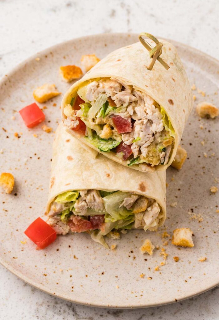 A wrap cut in half with chicken caesar salad inside of it.