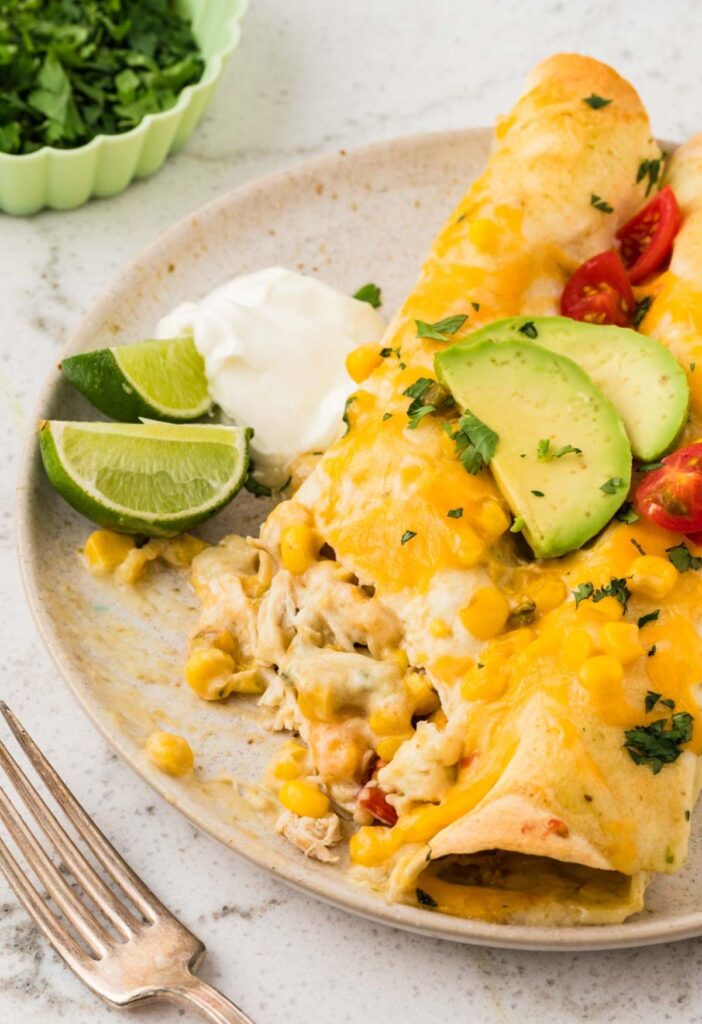 Two enchiladas with avocado and lime garnish and a fork on the plate.