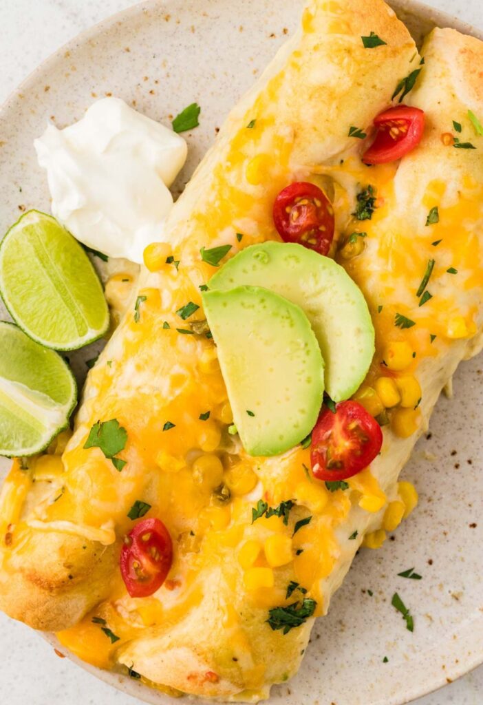 Two chicken enchiladas with green chili enchilada sauce on a serving plate.