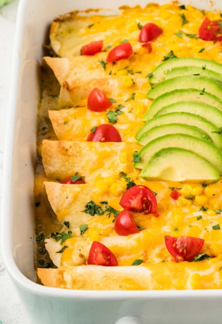 A white pan of chicken enchiladas topped with cheese, avocado, and corn.