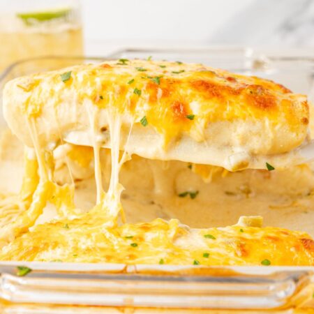 A pan of chicken enchiladas with sour cream sauce, and a spatula with an enchilada on it.