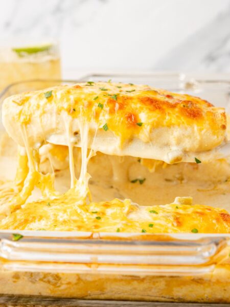 A pan of chicken enchiladas with sour cream sauce, and a spatula with an enchilada on it.