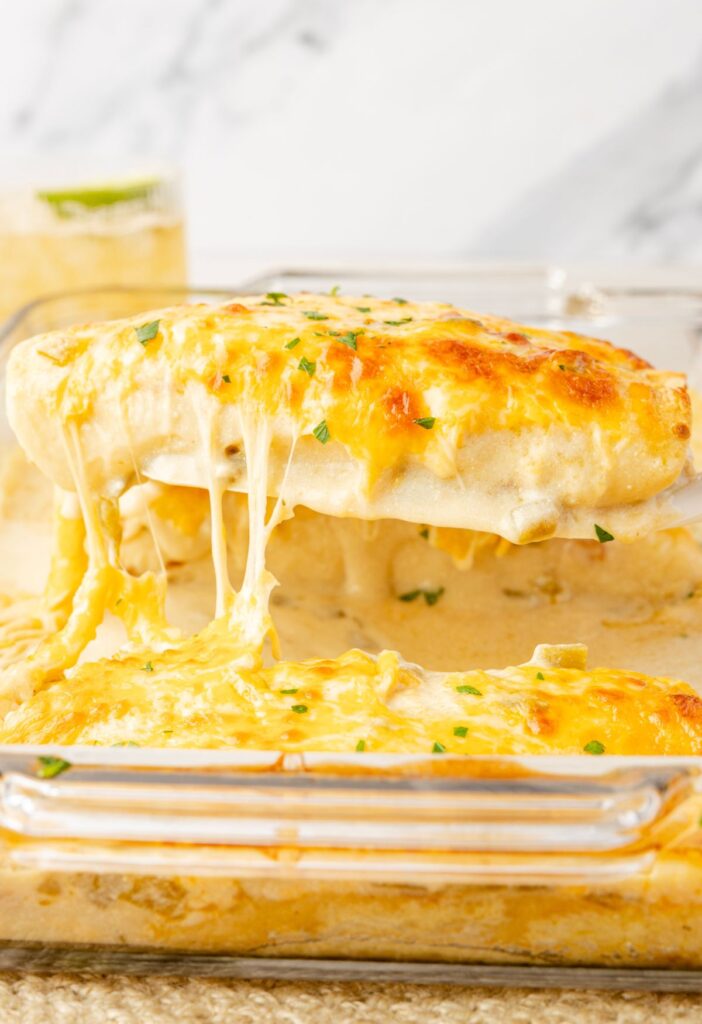 A pan of chicken enchiladas with sour cream sauce, and a spatula with an enchilada on it.