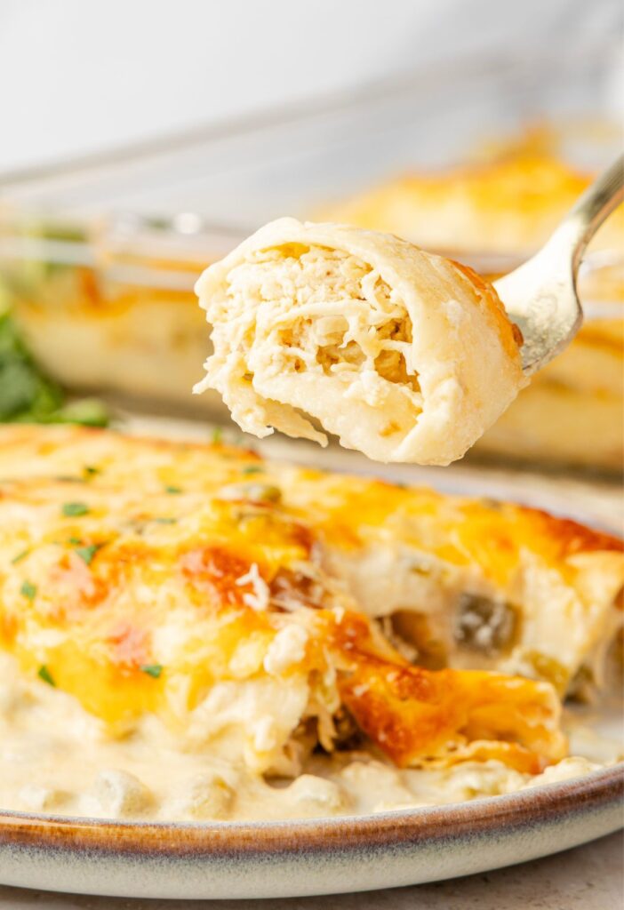 A serving plate with an enchilada on it and a fork with a bite on it.