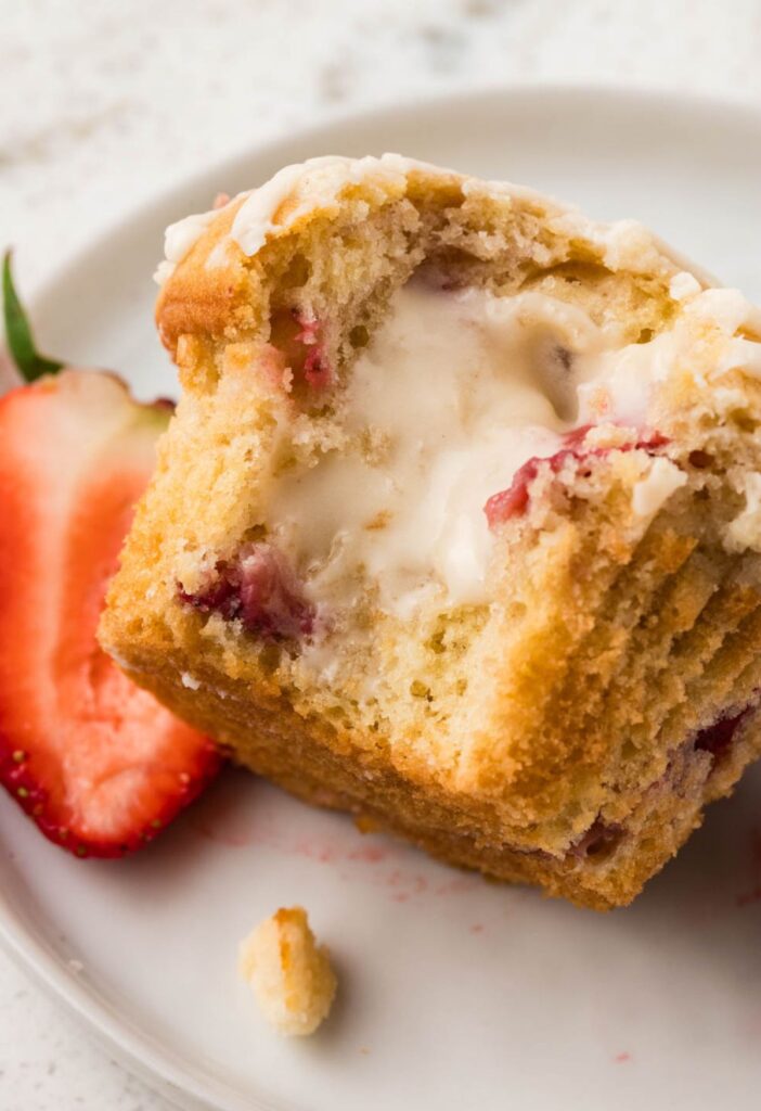 A muffin laying in it's side with it cut open to show the cheesecake cream cheese center.