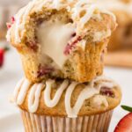 A stack of two muffins with the top one being cut in half to see the cream cheese center.