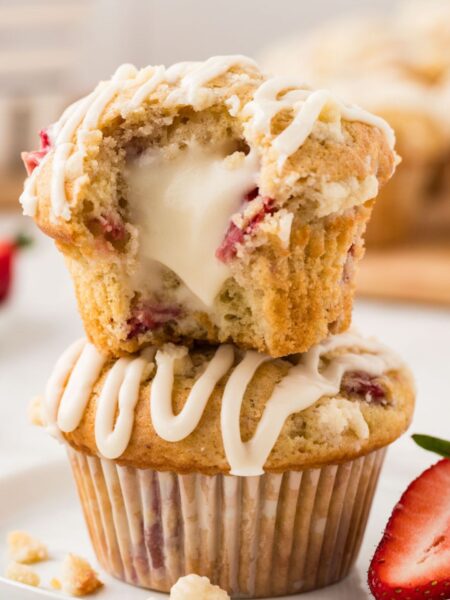 A stack of two muffins with the top one being cut in half to see the cream cheese center.