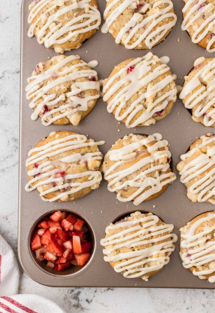Muffin tin of baked muffins with one taken out and filled with fresh strawberries.