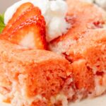 A slice of the strawberry cake with whipped cream and a strawberry on top of it.