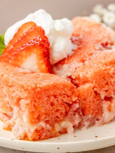 A slice of the strawberry cake with whipped cream and a strawberry on top of it.