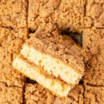 A top view of the baked coffee cake with a streusel topping and a piece turned on its side to see the middle.