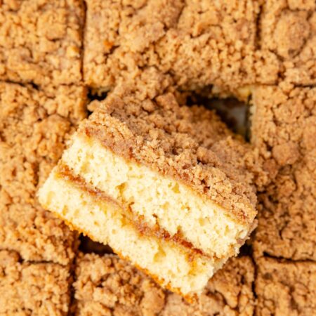 A top view of the baked coffee cake with a streusel topping and a piece turned on its side to see the middle.