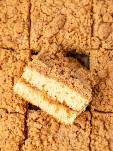 A top view of the baked coffee cake with a streusel topping and a piece turned on its side to see the middle.