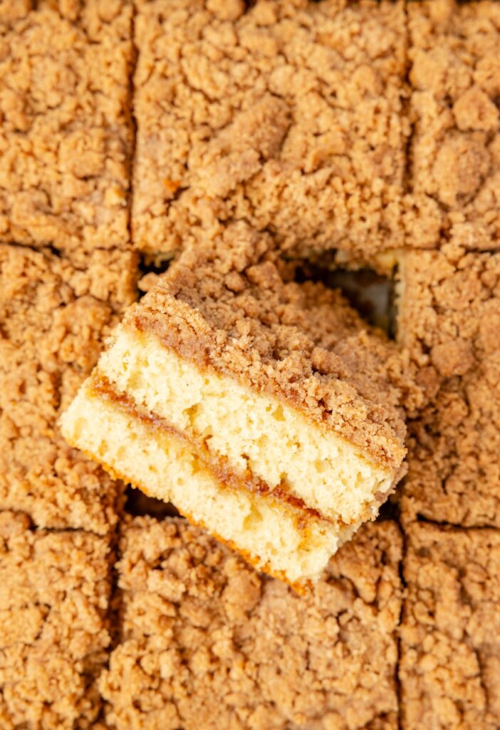 A top view of the baked coffee cake with a streusel topping and a piece turned on its side to see the middle.