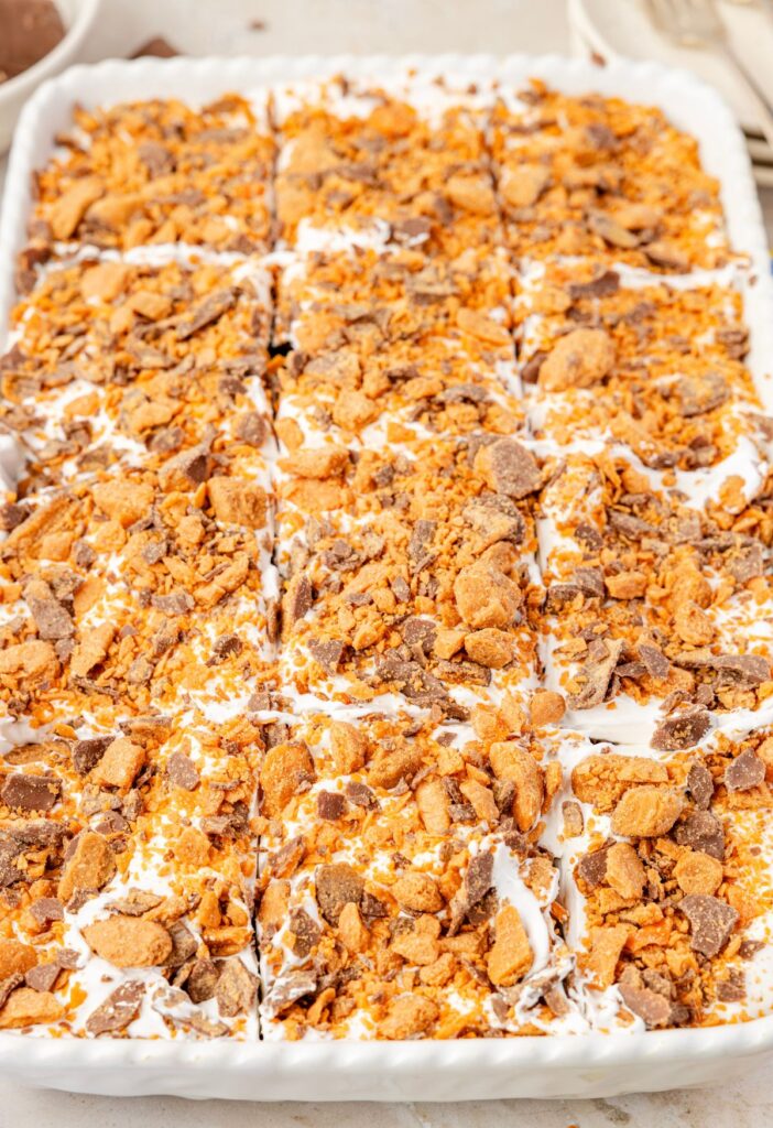 The cake pan with the cooked cake in it and topped with whipped cream and crushed butterfinger candy bars.