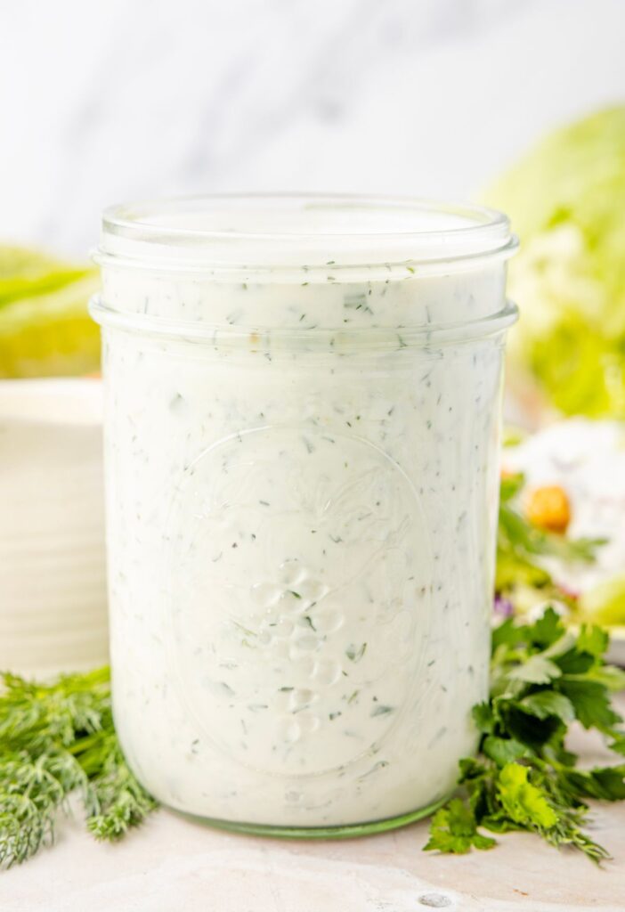 View of a glass jar full of ranch dressing with buttermilk and fresh herbs