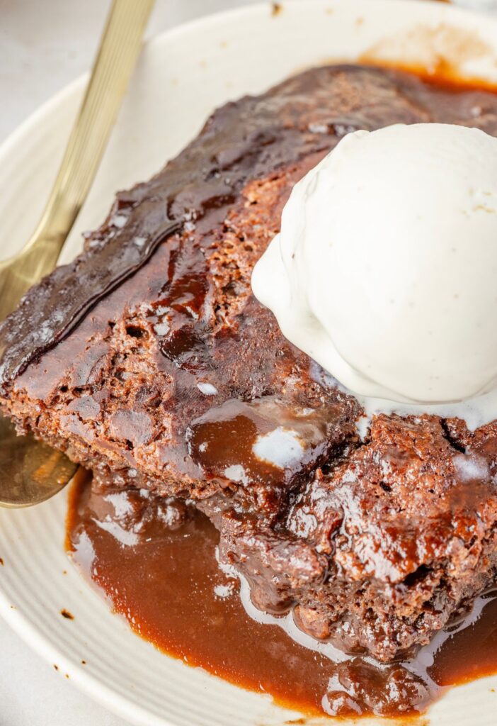 Hero image for the chocolate cobbler dessert on a white plate with a scoop of ice cream on top of it and a spoon.