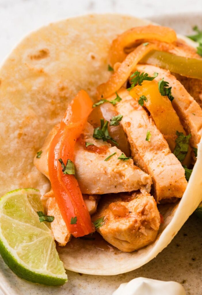 A flour tortilla with chicken fajita inside of it with a lime wedge.