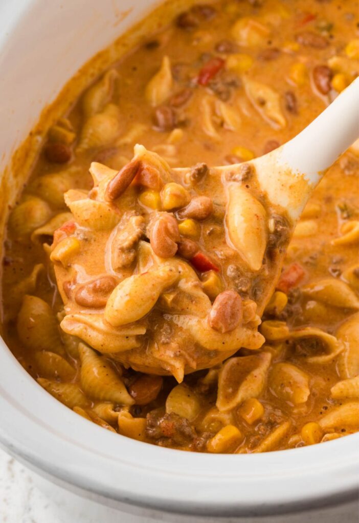 A slow cooker with a scoop inside of it of the cheesy taco pasta