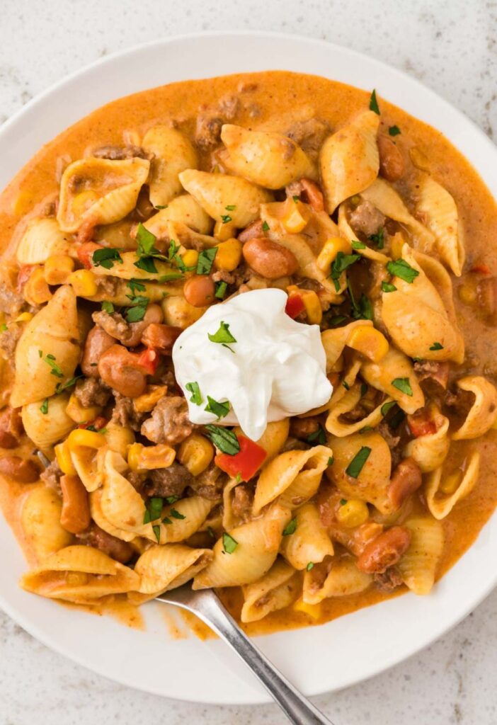 A white plate of the cheesy taco pasta with sour cream on top.