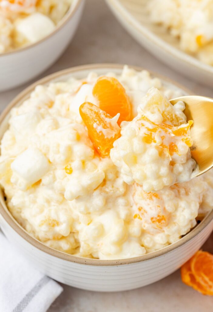 A bowl of the creamy fruit salad called frog eye salad and a spoon scooping some up.