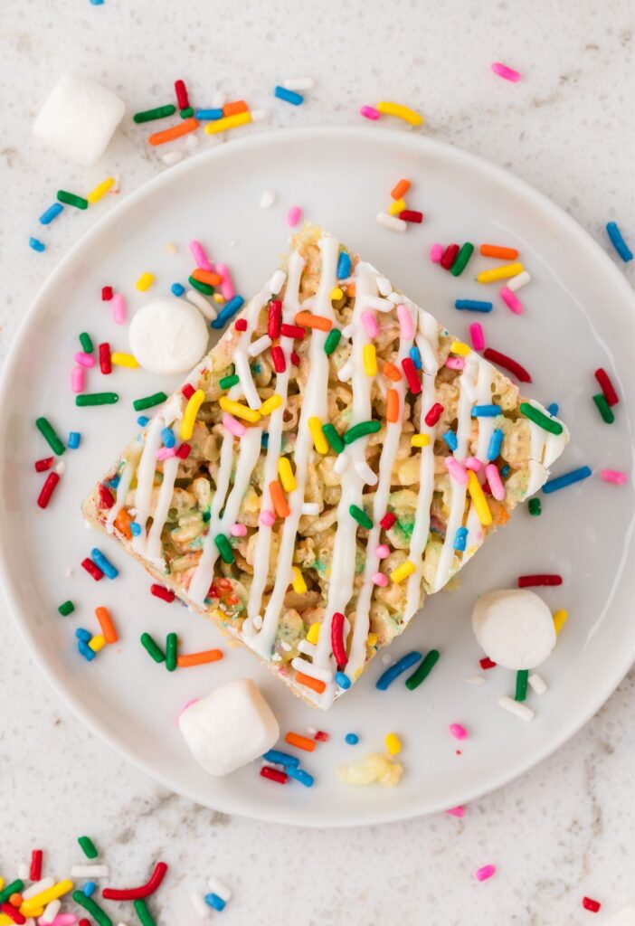 Top view of a rice krispie treat on a plate with marshmallows and sprinkles around it.