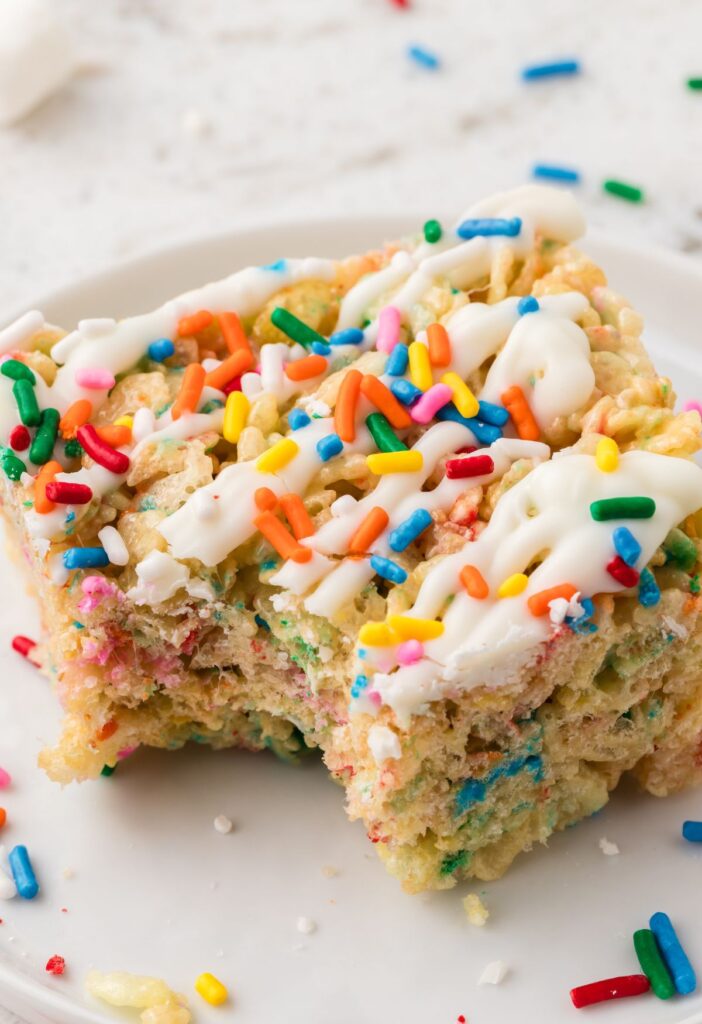 One Krispie treat with sprinkles and cake batter extract on a plate with a bite taken out of it.