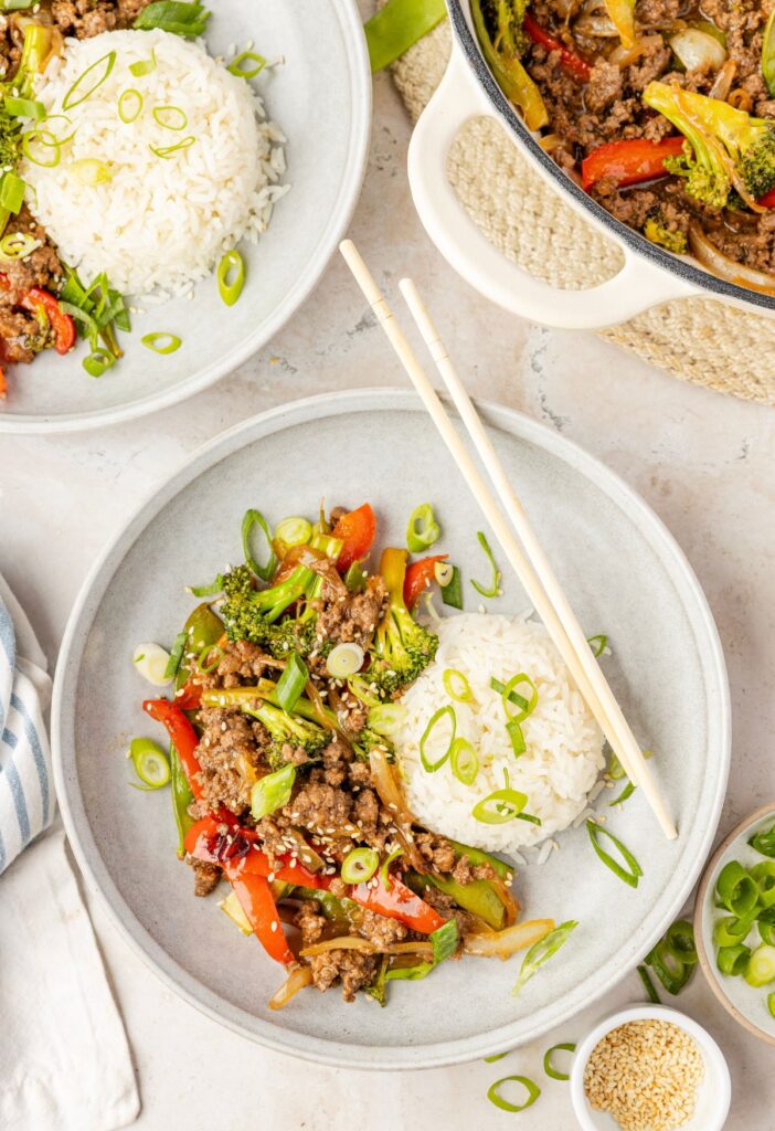 Overhead pic of the skillet with stir fry in it and a serving of it with some white rice and chopsticks