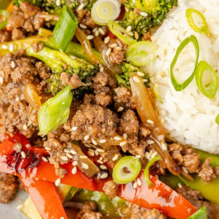 A plate of white rice and the ground beef stir with a sauce and green onions on top.