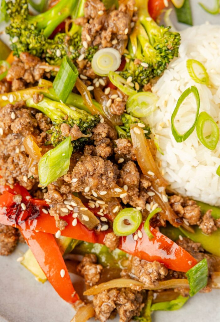 A plate of white rice and the ground beef stir with a sauce and green onions on top.