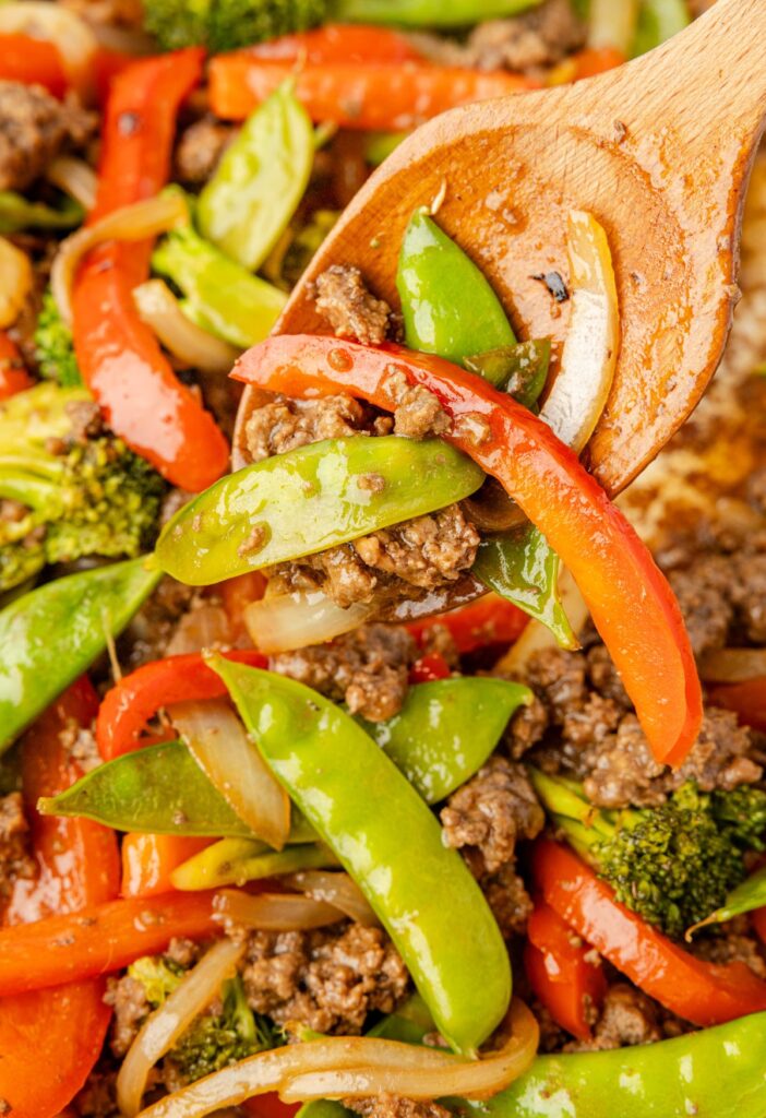 Close up of the ground beef stir fry with vegetables and a wooden spoon in the pan.