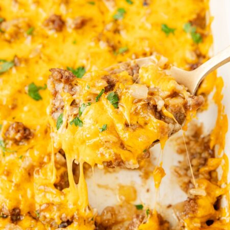 A close up of a spoon holding some of the cheesy rice casserole on it above the white pan of casserole.