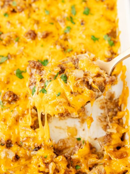 A close up of a spoon holding some of the cheesy rice casserole on it above the white pan of casserole.