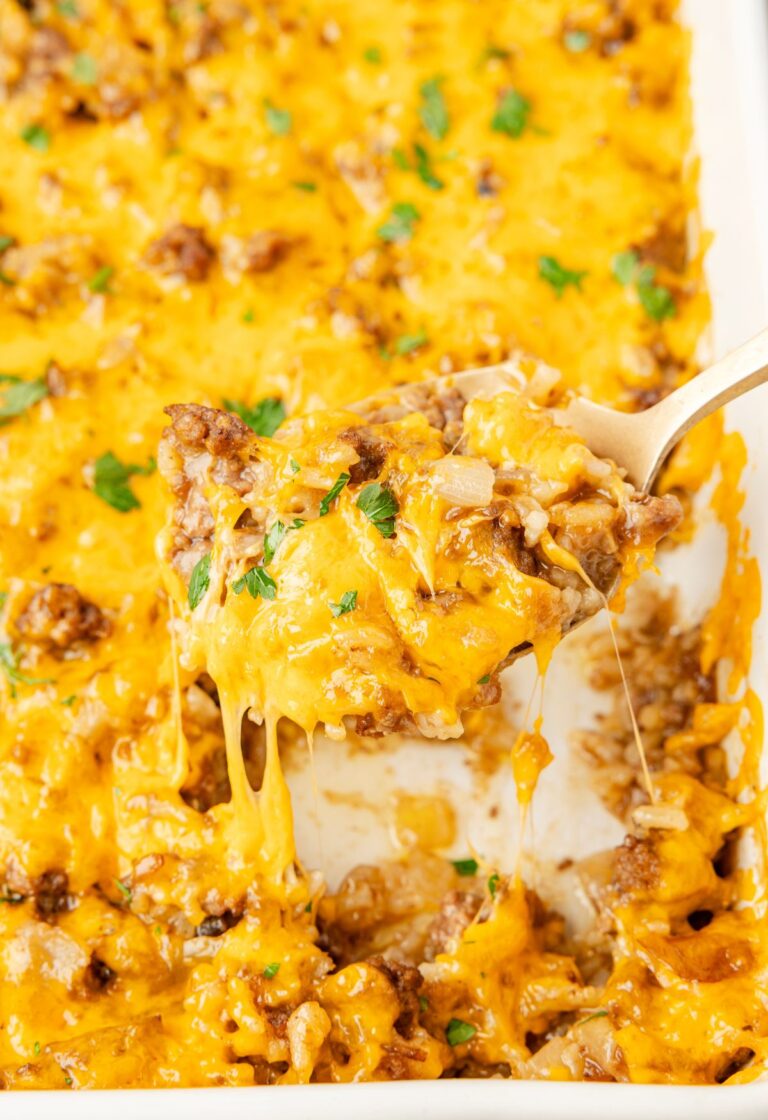 A close up of a spoon holding some of the cheesy rice casserole on it above the white pan of casserole.