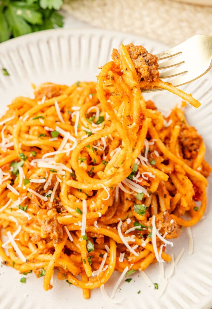 A fork holding some spaghetti on it above the serving plate of it.