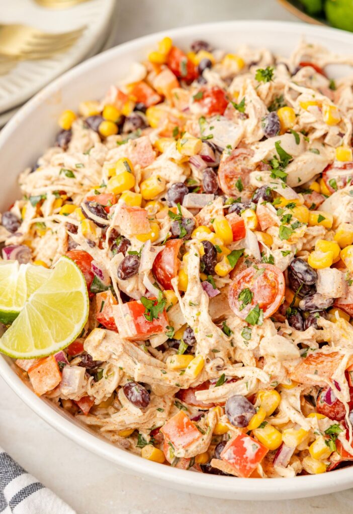 A white bowl of chicken salad with a lime wedge in the corner.