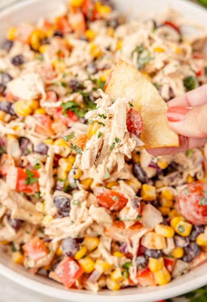 A bowl of the creamy chicken salad with a pita chip being dipped in