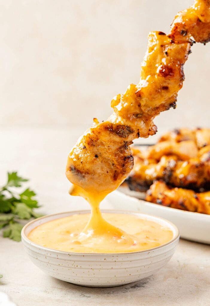 A bang bang chicken skewer being dipped into bang bang sauce inside a bowl.