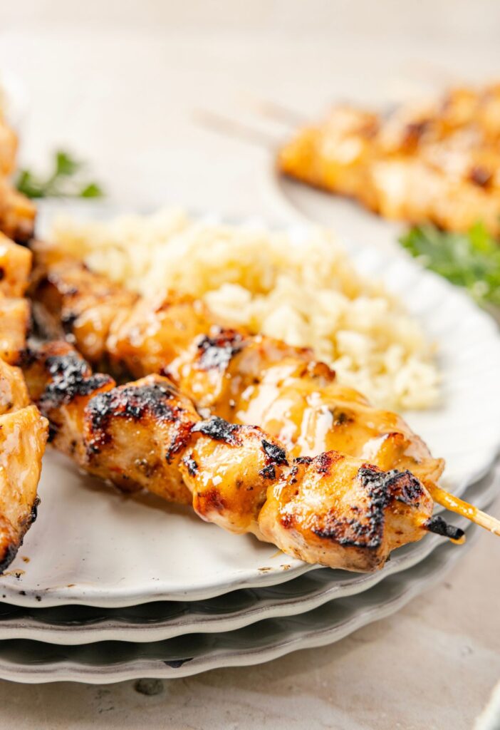 A plate of chicken skewers with rice next to them.