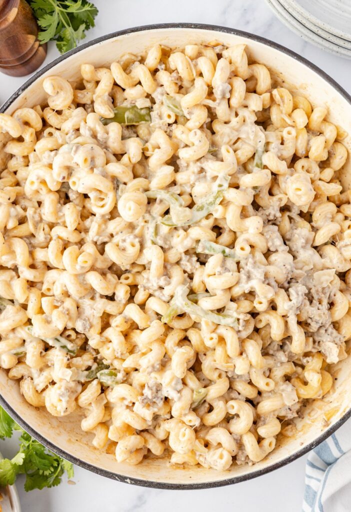 Skillet of the cooked cheesesteak pasta with ground beef and a cheesy sauce.