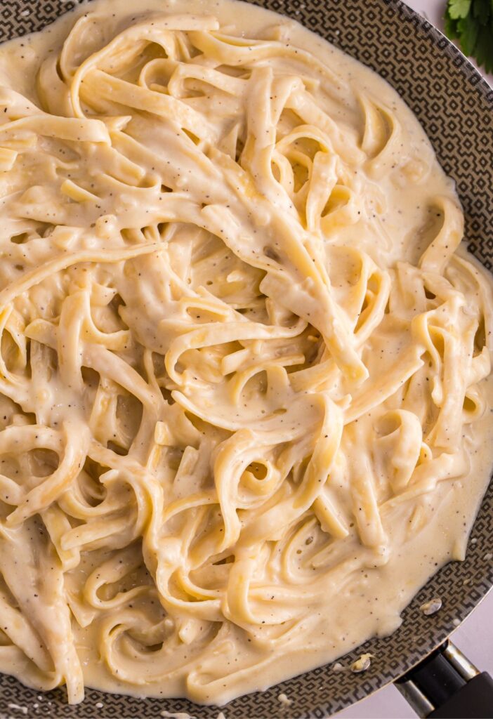 Skillet pan of creamy Alfredo sauce and fettuccine noodles.