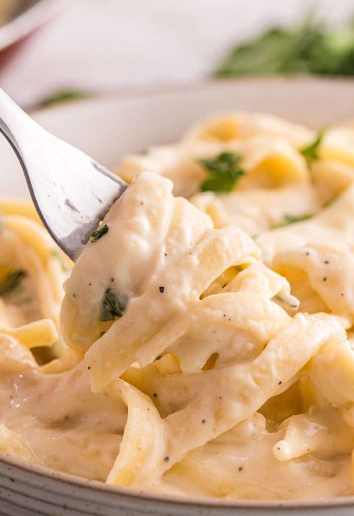 Alfredo sauce with fettuccine noodles being twirled on a fork.