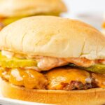 A burger with cheese and pickles and sauce, on a hamburger bun sitting on a plate with fries.