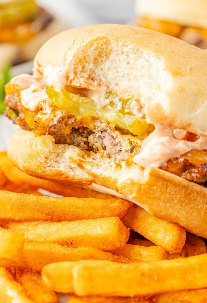 A cheeseburger with a bite taken out of it sitting in a tray with some fries for eating.