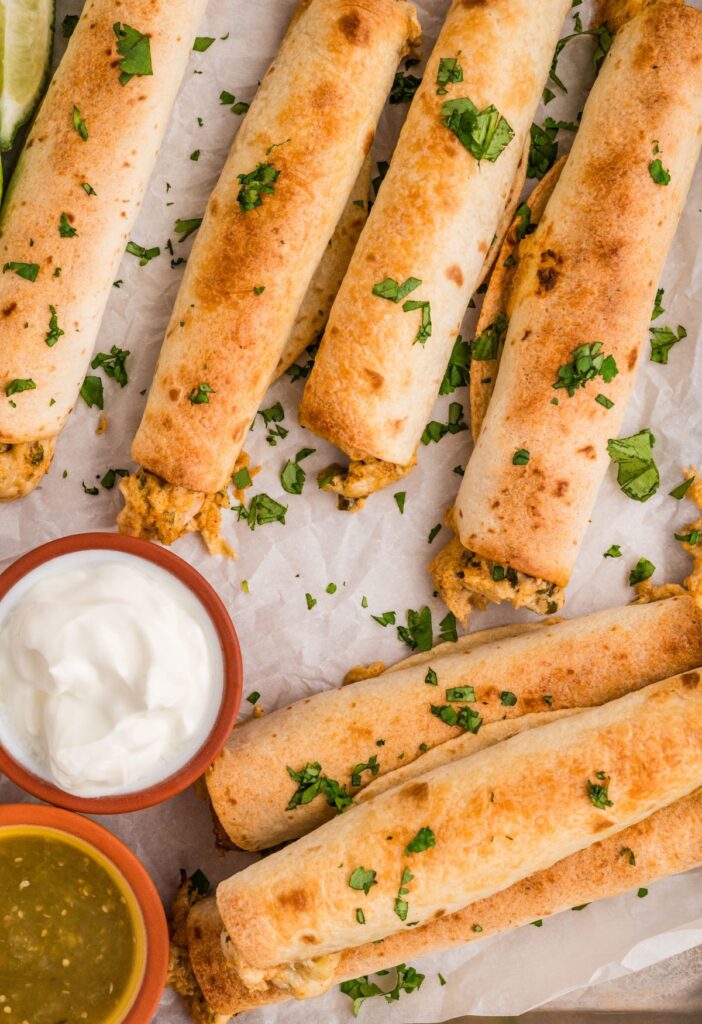 Chicken taquitos with dipping sauces on a baking sheet.