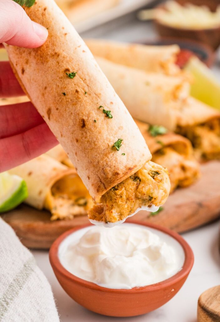 A chicken taquitos being dipped into sour cream