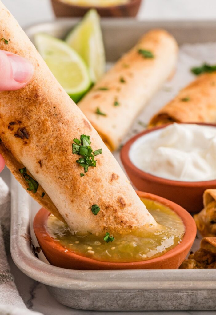 Chicken taquito being dipped in green sauce