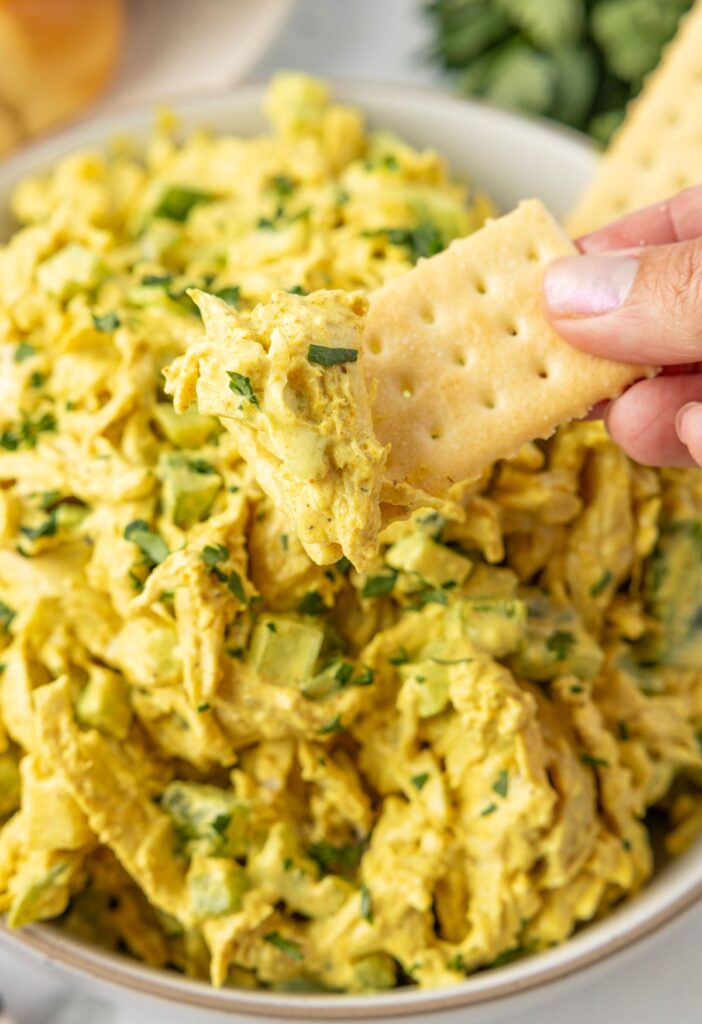 Chicken salad with a hand holding a cracker dipped into the chicken salad.