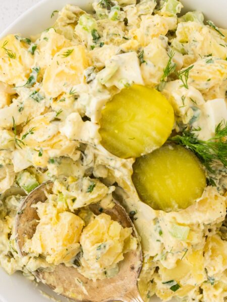 Top view of the potato salad, with dill pickle slices on top and a serving spoon.